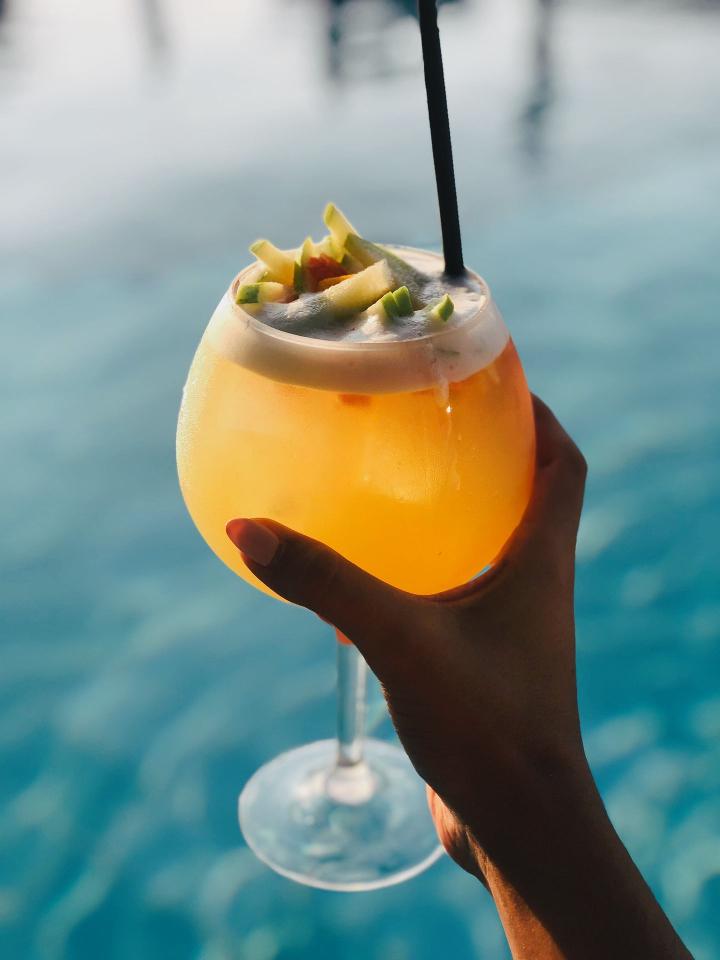 person holding clear drinking glass with yellow liquid